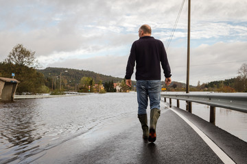 Man walking on the flooded road when the river Tovdalselva flooded in Drangsholt in Kristiansand, Norway - October 3, 2017.