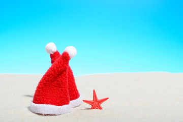 Two Santa hats next to a starfish on a sunny beach