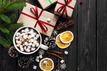 A cup of hot coffee with marshmallow, spruce branches, cones, Christmas gifts, mugs of orange, snowflakes, cinnamon. Traditional festive decoration Christmas dark background top view.
