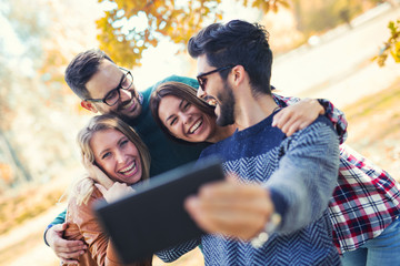 Group of four funny friends taking selfie with a smart phone in park