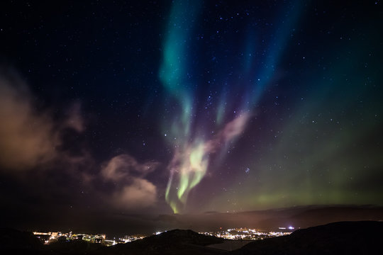 Aurora Borealis with shining stars on the sky over the mountains and highlighted city, Nuuk, Greenland