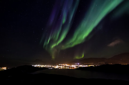 Aurora Borealis with shining stars on the sky over the mountains and highlighted city, Nuuk, Greenland