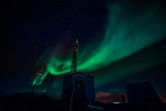 Green waves of Aurora Borealis with shining stars over the mountains and radio tower, Nuuk, Greenland