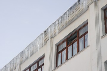 Large icicles hang on house roof. Winter cityscape