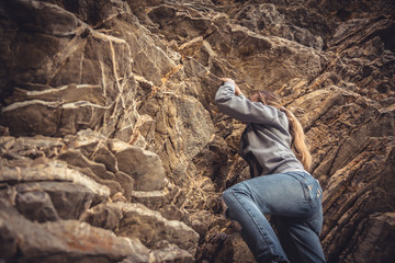Courage woman achieving her goal climbing up on rock 