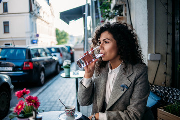 the girl in the cafe drinks water, curly serious woman relaxes