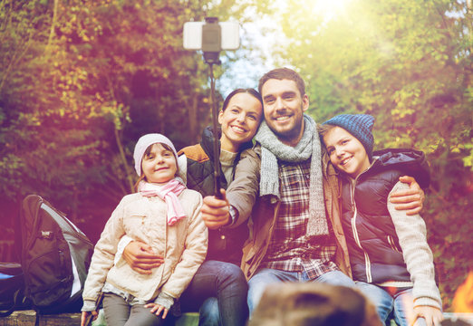 family with smartphone taking selfie near campfire