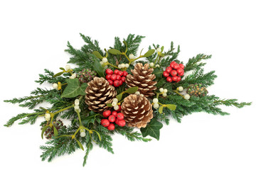 Christmas floral table decoration with holly, gold pine cones, ivy, mistletoe, cedar and juniper leaf sprigs on white background.