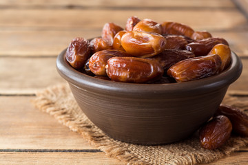 Dried dates fruit in ceramic bowl on wooden table.