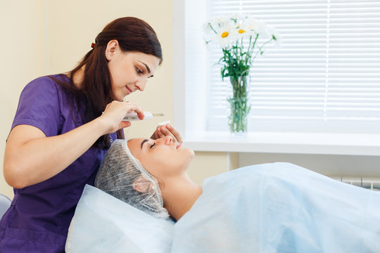 The doctor-cosmetologist makes the apparatus a procedure of ultrasound cleaning of the facial skin of a beautiful, young woman in a beauty salon. Cosmetology and professional skin care.