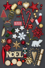 Noel sign with symbols of christmas including bauble decorations, holly, mistletoe, mince pies, foil wrapped chocolates and gingerbread biscuits on grey background.