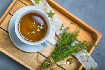 Healthy thyme tea in white cup on a wooden tray top view. Bokeh. Close up