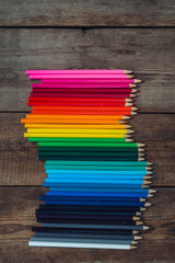 Fototapeta premium Colored pencils in gradient order located in the center on wooden table. School concept. Copy space