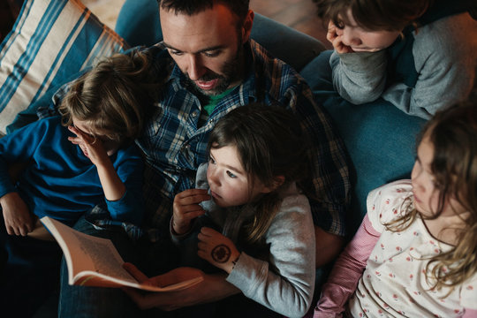 Young dad reading to kids on cozy couch