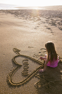 Girl writing word mom in sand on beach