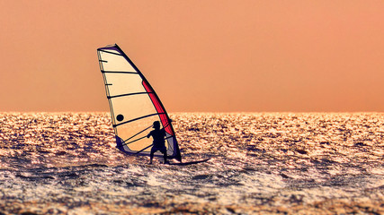 Windsurfer silhouette against a sunset background. Windsurfer Surfing The Wind On Waves, Recreational Water Sports, Extreme Sport Action. Recreational Sporting Activity. Healthy Active Lifestyle.