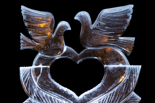 Ice sculpture with a heart and doves. with the flames behind warm.