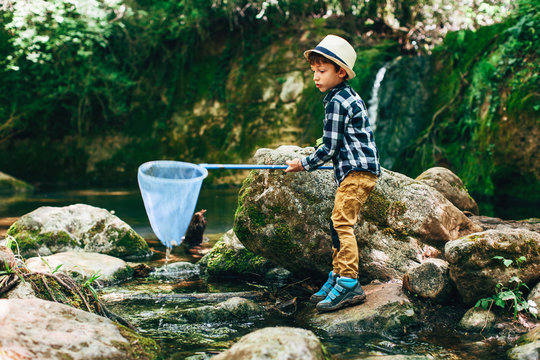Young boy using a blue net to catch fish in a river.