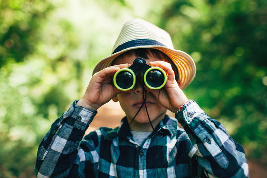 Young boy looking through binoculars in a forest.