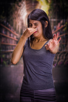 Beautiful and lonely girl suffering from anorexy, holding in her hand a piece of chocolate and covering her nose to do not smell the chocolate, in a blurred background