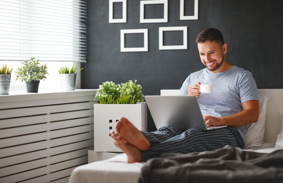 happy young man with laptop and cup of coffee in  the bed