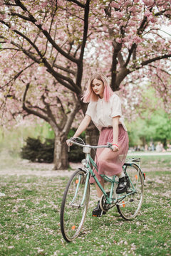 Girl with a pink hair with the bike in the blossoming park