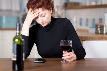 Upset woman drinking wine at home holding her head, looking depressed and sad
