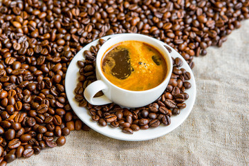 Cup of coffee and coffee beans on the background of a bag. Hot coffee.