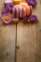 Violet and yellow macarons and flowers on wooden table background. Colorful french dessert with fresh flowers. Autumn concept