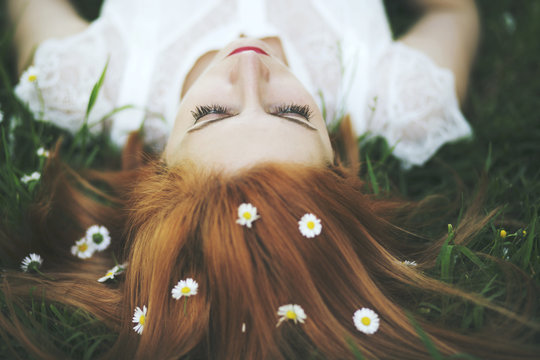 Ginger haired woman laying on grass with chamomile in her hair