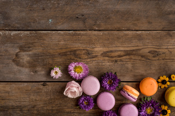 Macarons and flowers on the background of a wooden table. Colorful French dessert with fresh flowers. Gradient between purple and yellow. Place for text