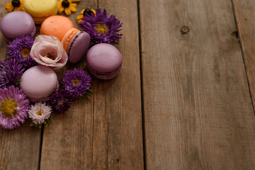 Fototapeta na wymiar Violet and yellow macarons and flowers on wooden table background. Colorful french dessert with fresh flowers. Autumn concept