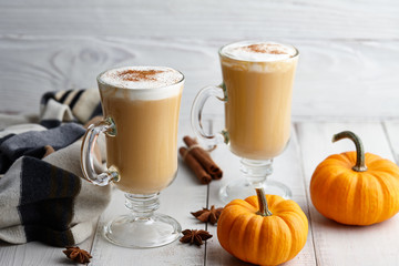Fall pumpkin spice latte with whipped cream and cinnamon, ornamental pumpkins and warm woolen scarf on white wooden background