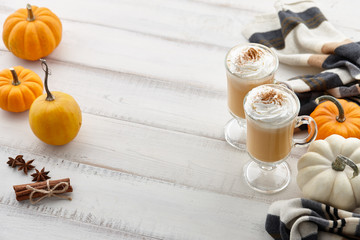 Fall pumpkin spice latte with whipped cream and cinnamon, ornamental pumpkins and warm woolen scarf on white wooden background, copyspace