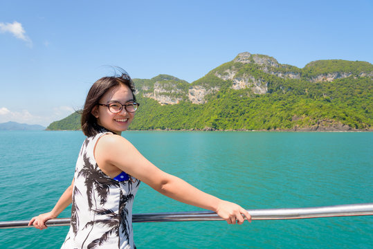 Asian young woman with eyeglasses smiling happily on the boat while cruising the beautiful natural of the blue sea and sky in summer at Mu Ko Ang Thong National Park, Surat Thani, Thailand