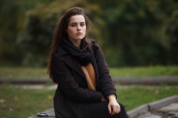 Naklejka na ściany i meble Young woman wearing stylish checkered coat and knitted sweater sitting on the bench in the autumn park. Youth, fall, casual style