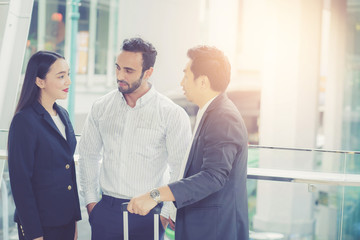 Two handsome young businessmen and lady in classic suits are holding cups of coffee, talking and smiling, standing outside the office building.