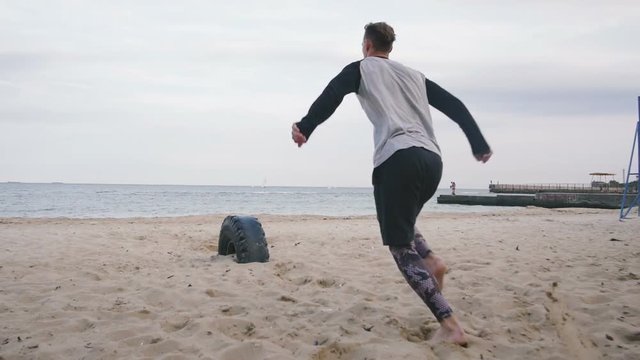 Young man doing parkour tricks on the beach near the sea