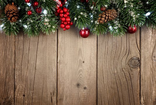 Christmas branch top border with berries and pine cones on a rustic old wood background
