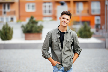 Outdoor portrait of handsome young man walking on the street, looking at camera and smile