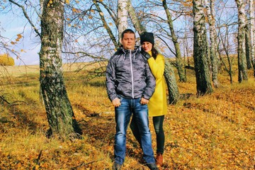 Autumn time: young couple posing against a background of autumn birch forest.