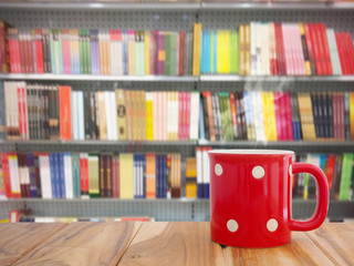 coffee on wooden table over books on shelves blur background.
