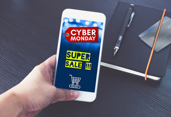 Cyber monday sale tag with shopping cart on mobile screen,Hand holding smart phone over black book and credit card to shop online in apps,E-commerce concept