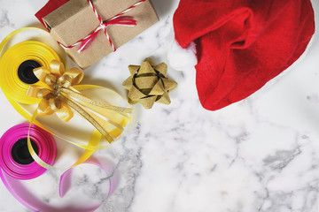 Christmas gifts preparation on white marble table with copy space. Red santa hat with gift box and colorful ribbon