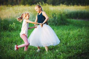 Two little girls playing in the garden in good Sunny warm day, wearing the same dress. Adorable children having fun outdoors, dancing in the meadow