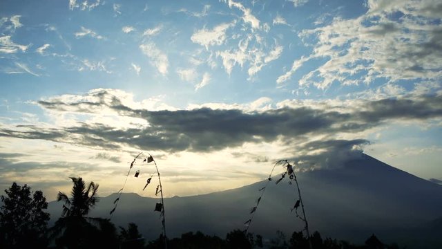 Two penjors are swaying in the wind on the background of tranquil landscape with volcano Gunung Agung, Bali, Indonesia. Penjor is the decorative bamboo pole