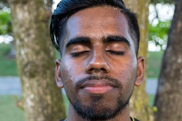 Close up portrait of young smiling asian indian yoga man outside. Park, beachside. Bali island.