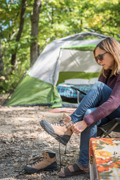 Woman Putting On Hiking Boots At Campsite With Tent In Background