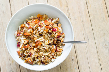 Breakfeast musli with dried fruits,nuts and oats served in white bowl, wooden background, top view.