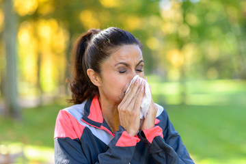 Woman blowing her nose on a tissue outdoors